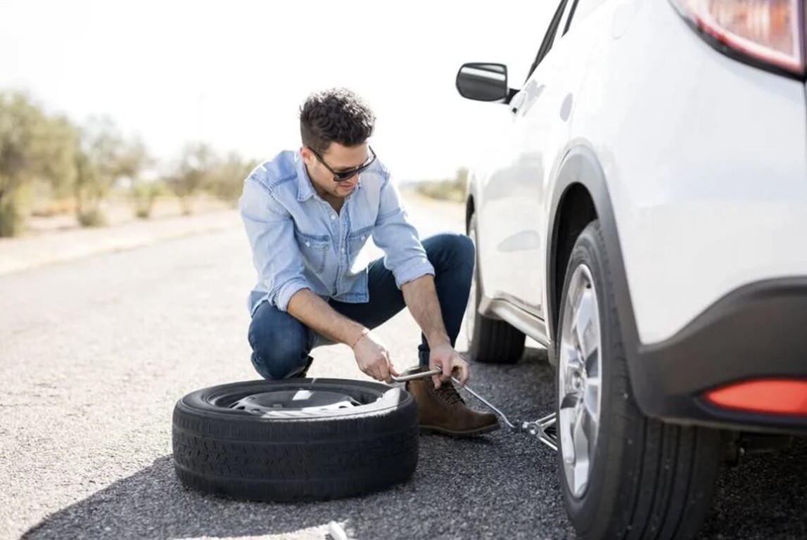 Driver changing a flat tire on a white SUV on the roadside near Copiague, NY