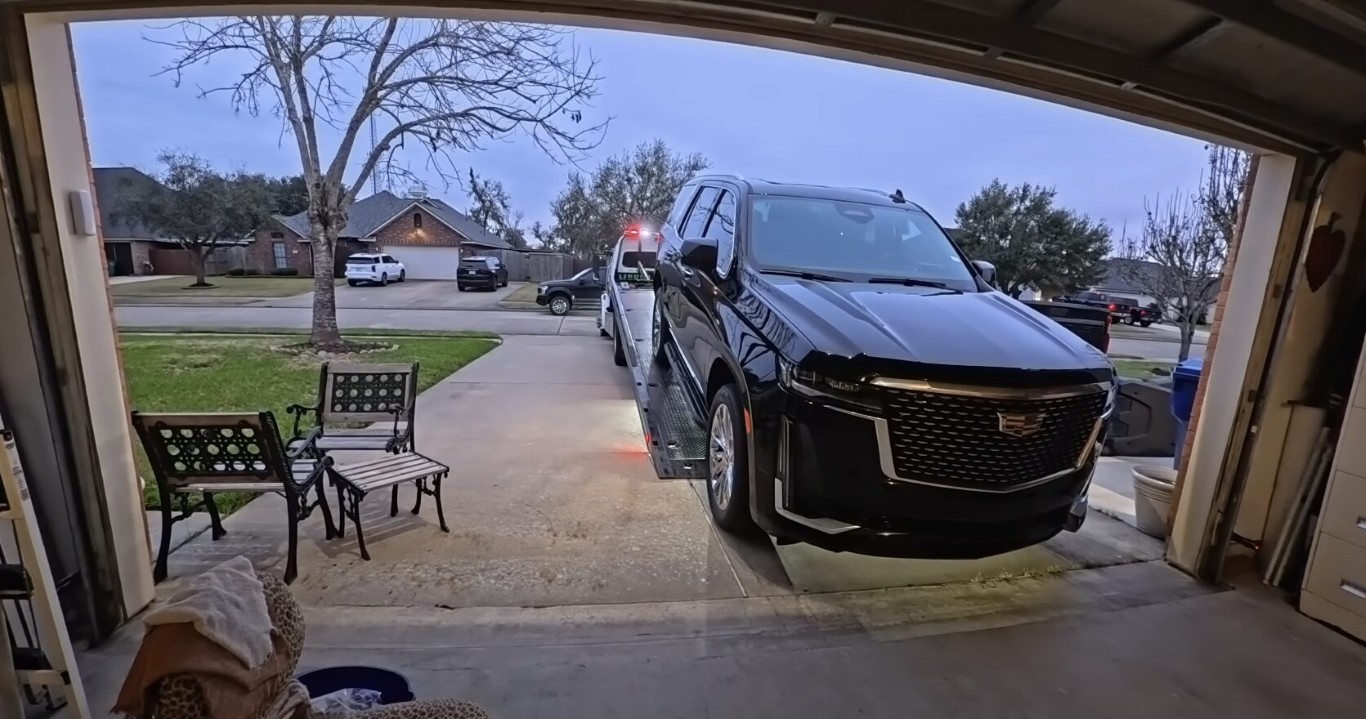Tow truck loading a black Cadillac Escalade onto a flatbed at a residential driveway in Copiague, NY