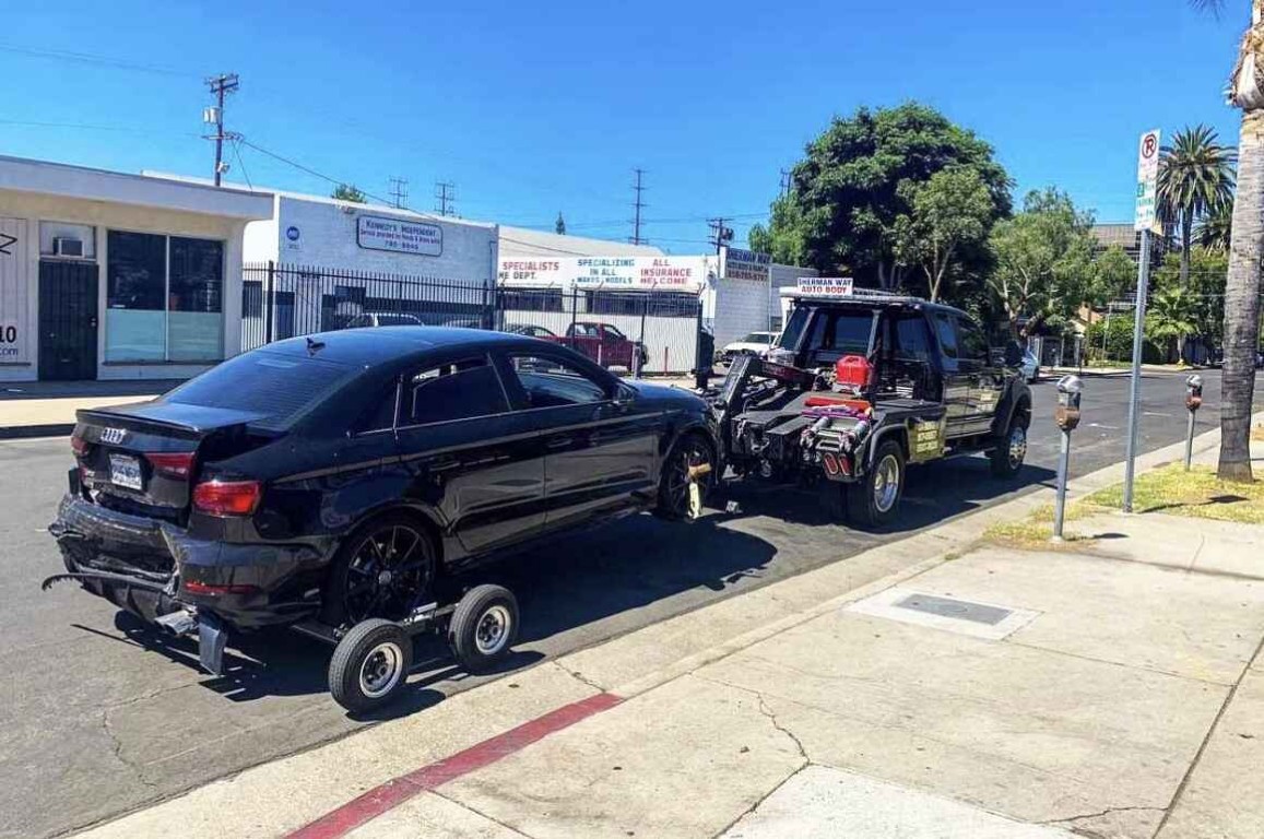 Wheel-lift tow truck towing a black Audi on a city street in Copiague, NY